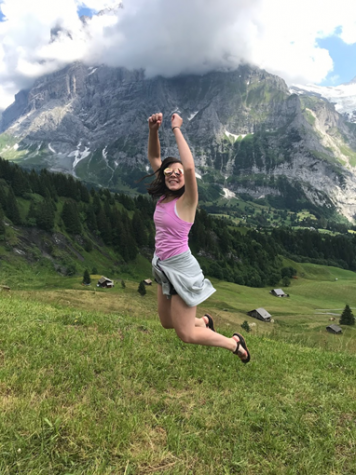 Kate Caviezel, a young woman, jumping in a field in the Swiss Alps.